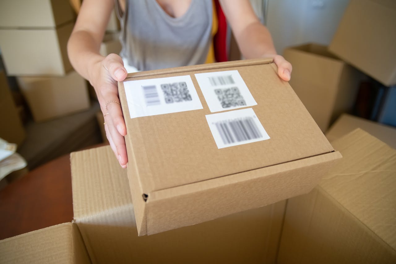 why-choose-us Close-up of a person holding a cardboard box with barcode labels, indoors setting.